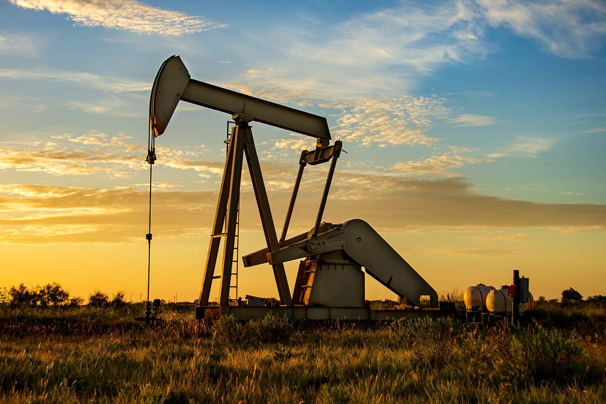 Oil pumpjack operating in an open field at sunset